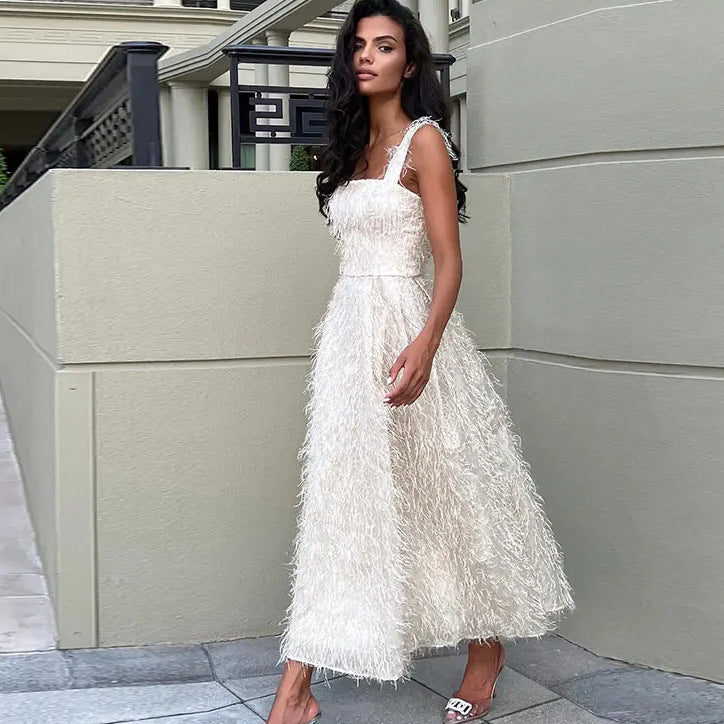 Frau in elegantem, weißem Abendkleid mit Federmuster, steht auf Gehweg vor modernem Gebäude. Mode, Abendkleid, Damenmode, elegantes Outfit.