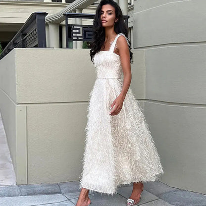 Frau in elegantem, weißem Abendkleid mit Federmuster, steht auf Gehweg vor modernem Gebäude. Mode, Abendkleid, Damenmode, elegantes Outfit.
