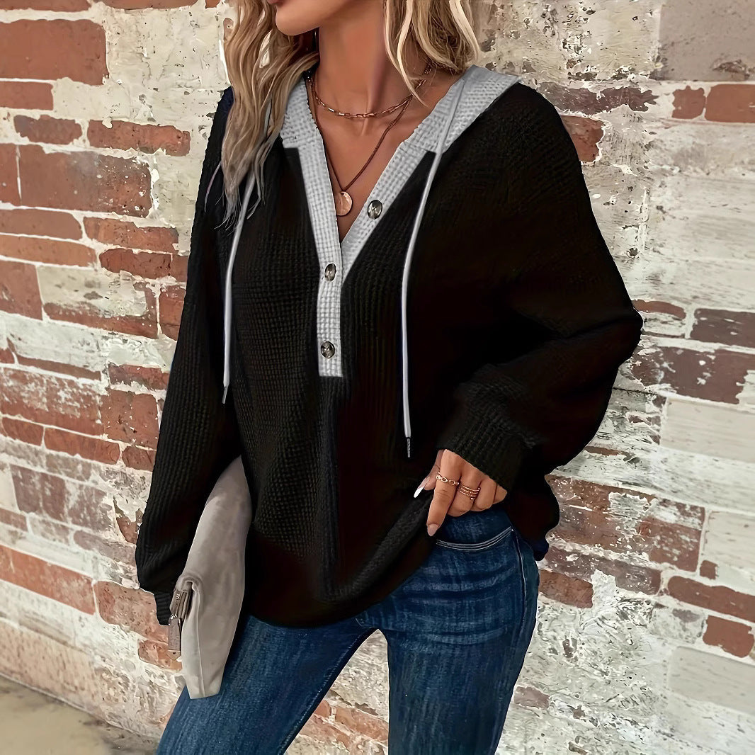 Frau in schwarzem Kapuzenpullover mit Knöpfen und blauer Jeans vor Backsteinwand. Modetrend, lässiger Stil, Herbstmode.