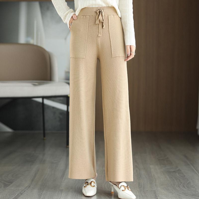 Damenhose beige, weites Bein, hoher Bund, Kordelzug, Taschen, eleganter Look, kombiniert mit weißem Pullover und Schuhen, modernes Wohnzimmer.