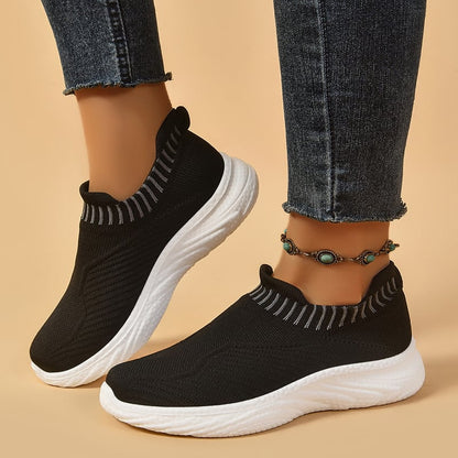 Schwarze Damen-Sneaker mit weißer Sohle, getragen mit Jeans und einem türkisfarbenen Fußkettchen. Bequeme, modische Schuhe für Freizeit und Sport.