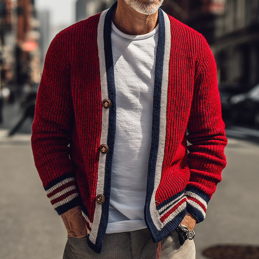 Älterer Mann in roter Strickjacke mit weißen und blauen Streifen, weißem T-Shirt und grauer Hose, steht auf einer städtischen Straße. Mode, Herrenbekleidung.