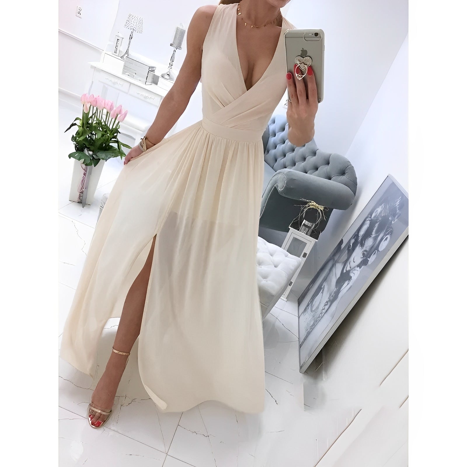 Elegantes cremefarbenes Abendkleid mit tiefem Ausschnitt und Beinschlitz, getragen von Frau im modernen Wohnzimmer mit Blumen und Kunstwerk.