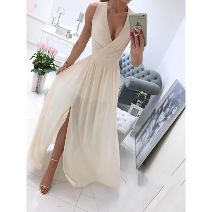 Elegantes cremefarbenes Abendkleid mit tiefem Ausschnitt und Beinschlitz, getragen von Frau im modernen Wohnzimmer mit Blumen und Kunstwerk.