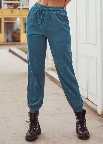 Frau in blauer Jogginghose und schwarzen Stiefeln vor weißer Tür. Modetrend, Freizeitkleidung, bequeme Damenmode, urbaner Stil.