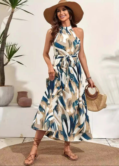 Frau in sommerlichem Maxikleid mit abstraktem Muster, Strohhut und Sandalen, hält runde Strohtasche. Perfekt für Strandmode und Sommeroutfits.
