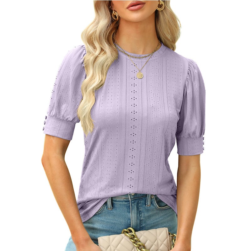 Blonde Frau in lila Spitzenbluse mit Puffärmeln, trägt goldene Halsketten und hält eine beige gesteppte Handtasche. Modetrend, Damenmode, Sommeroutfit.