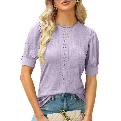Blonde Frau in lila Spitzenbluse mit Puffärmeln, trägt goldene Halsketten und hält eine beige gesteppte Handtasche. Modetrend, Damenmode, Sommeroutfit.