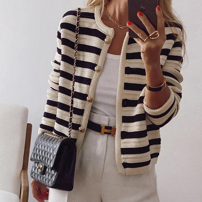 Frau in gestreifter Strickjacke mit goldenen Knöpfen, weißem Top, weißer Hose und schwarzer gesteppter Handtasche, macht Selfie.