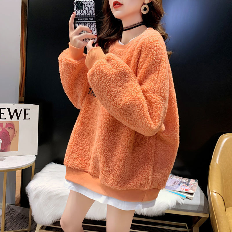 Frau in orangefarbenem Teddy-Fleece-Pullover, modisch kombiniert mit weißem Rock und schwarzem Choker, hält Smartphone. Trendige Herbstmode.