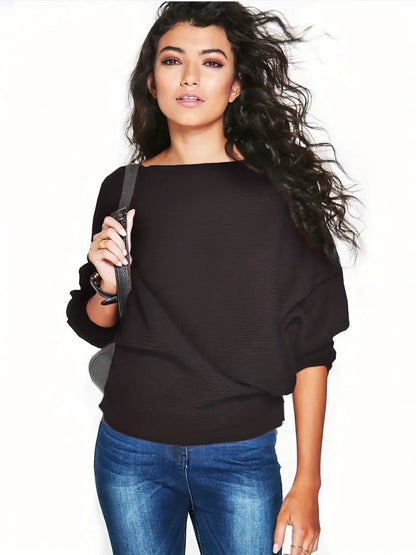 Junge Frau mit lockigem Haar trägt schwarzen Pullover und blaue Jeans, posiert selbstbewusst vor weißem Hintergrund. Mode, Freizeitkleidung, Stil.