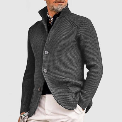 Eleganter Mann in grauem Strickblazer, kombiniert mit schwarzem Hemd und beiger Hose. Stilvolle Herrenmode, modern und zeitlos.