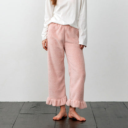 Frau in rosa Plüschhose mit Rüschen, weißem Langarmshirt, barfuß auf Holzboden. Bequeme Damenmode, gemütliche Loungewear, stilvolle Freizeitkleidung.