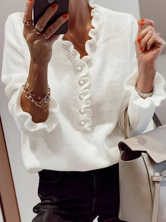 Frau in weißem Rüschenpullover mit Perlenknöpfen, hält Smartphone, trägt silberne Armbänder und hat eine graue Handtasche. Elegante Mode, Herbsttrends.