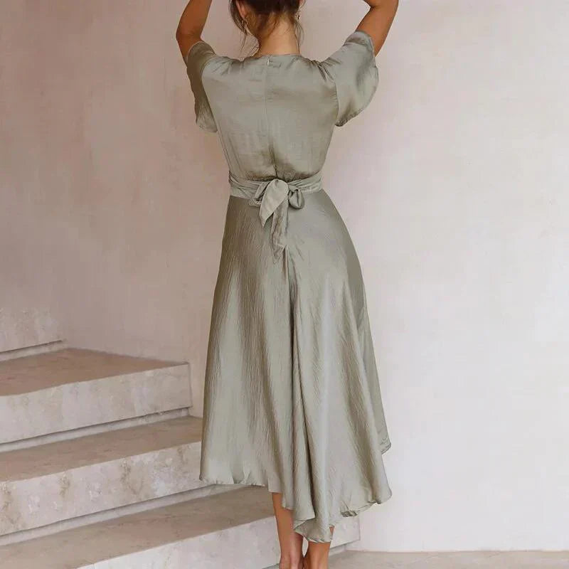 Frau in elegantem, olivgrünem Kleid mit Rückenausschnitt und Schleife, steht auf Treppe. Modetrend, Damenmode, Sommerkleid, stilvoll.
