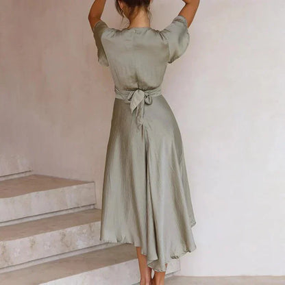 Frau in elegantem, olivgrünem Kleid mit Rückenausschnitt und Schleife, steht auf Treppe. Modetrend, Damenmode, Sommerkleid, stilvoll.