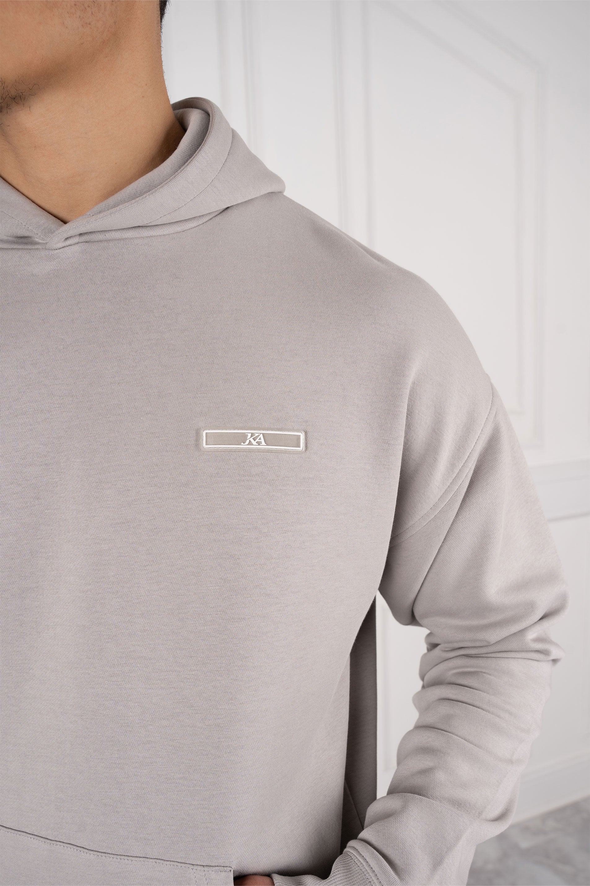 Grauer Hoodie mit dezentem Logo auf der Brust, getragen von einer Person. Moderner, minimalistischer Stil, ideal für lässige Mode und Streetwear.