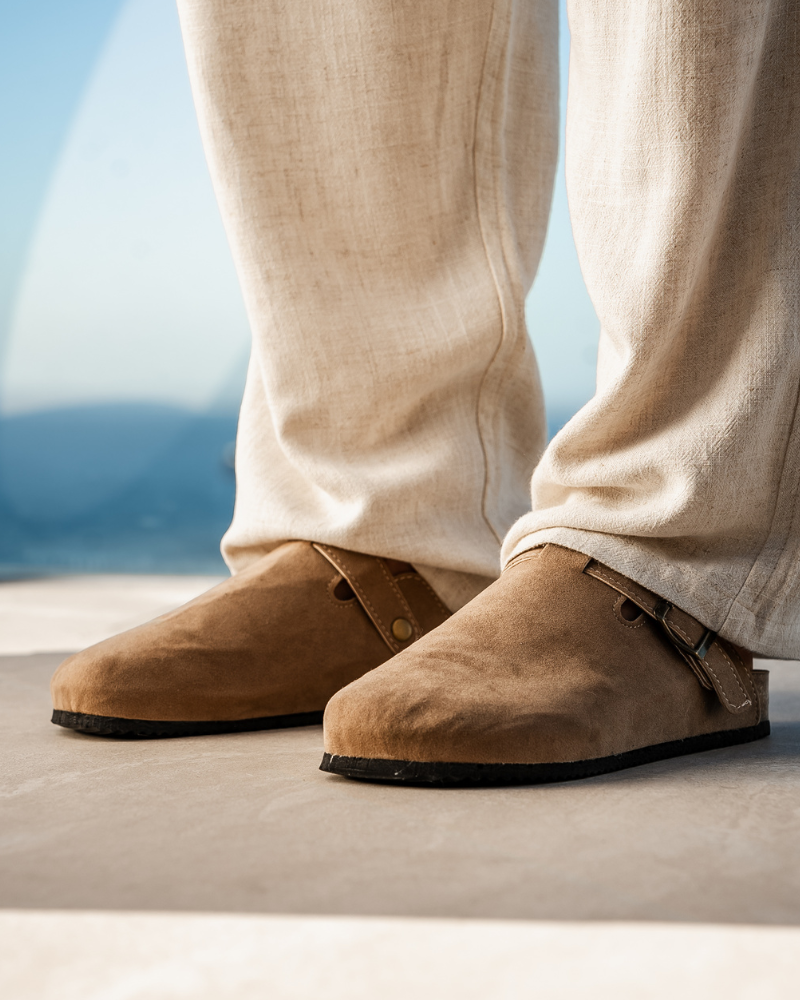 Beige Wildleder-Clogs auf einem Balkon, getragen mit hellen Leinenhosen. Stilvolle, bequeme Schuhe für den Sommer. Ideal für Freizeitmode.