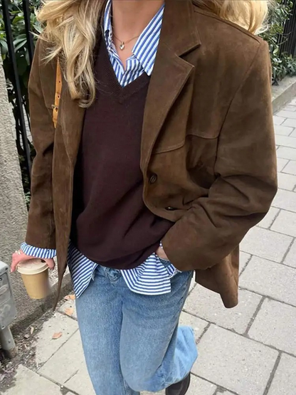 Frau in brauner Wildlederjacke, gestreiftem Hemd und Jeans hält Kaffeebecher. Modischer Herbstlook, Streetstyle, lässige Damenmode.
