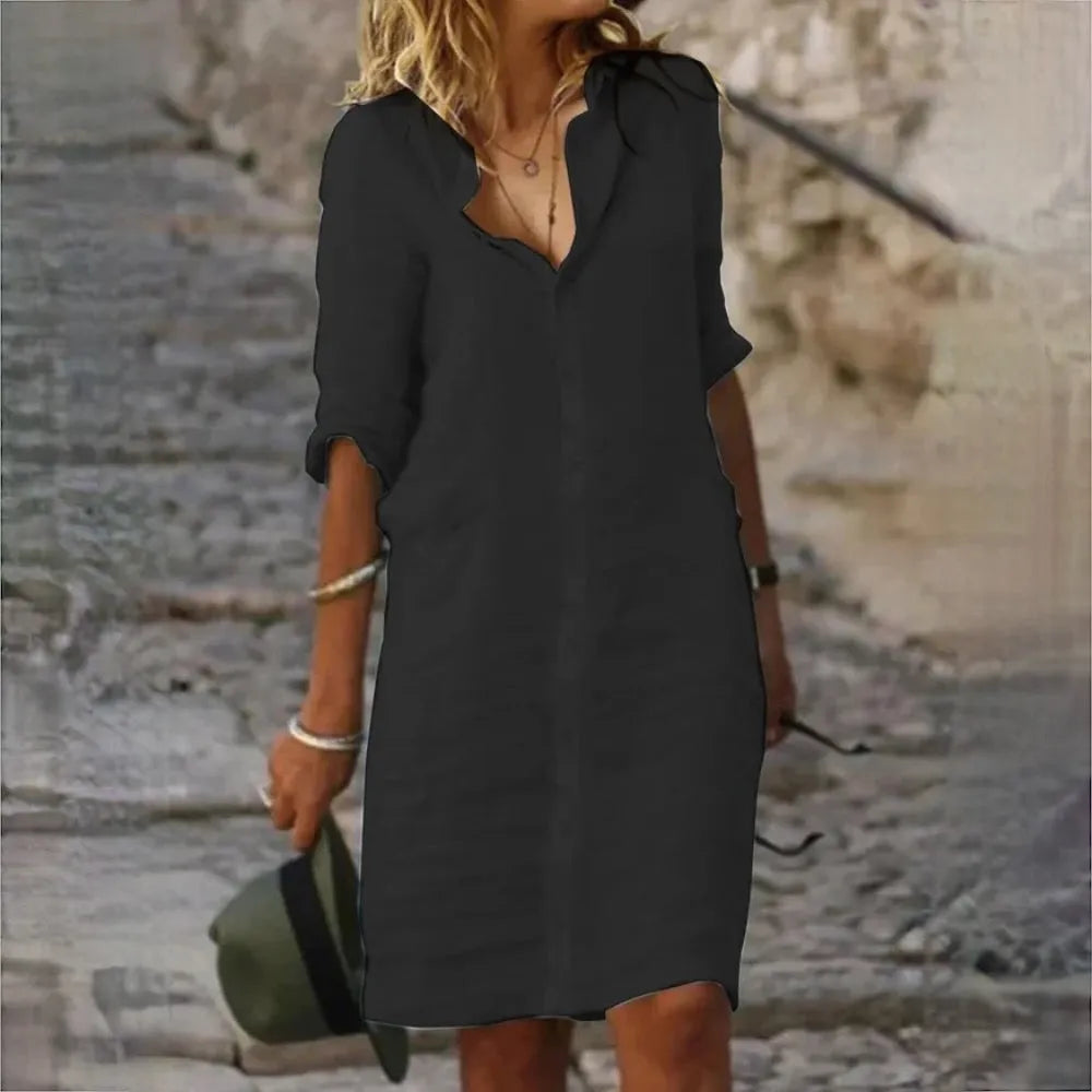 Frau in schwarzem Hemdkleid, hält Hut, geht auf steinigem Weg. Sommermode, lässiger Stil, Outdoor, Damenbekleidung, Freizeitlook.