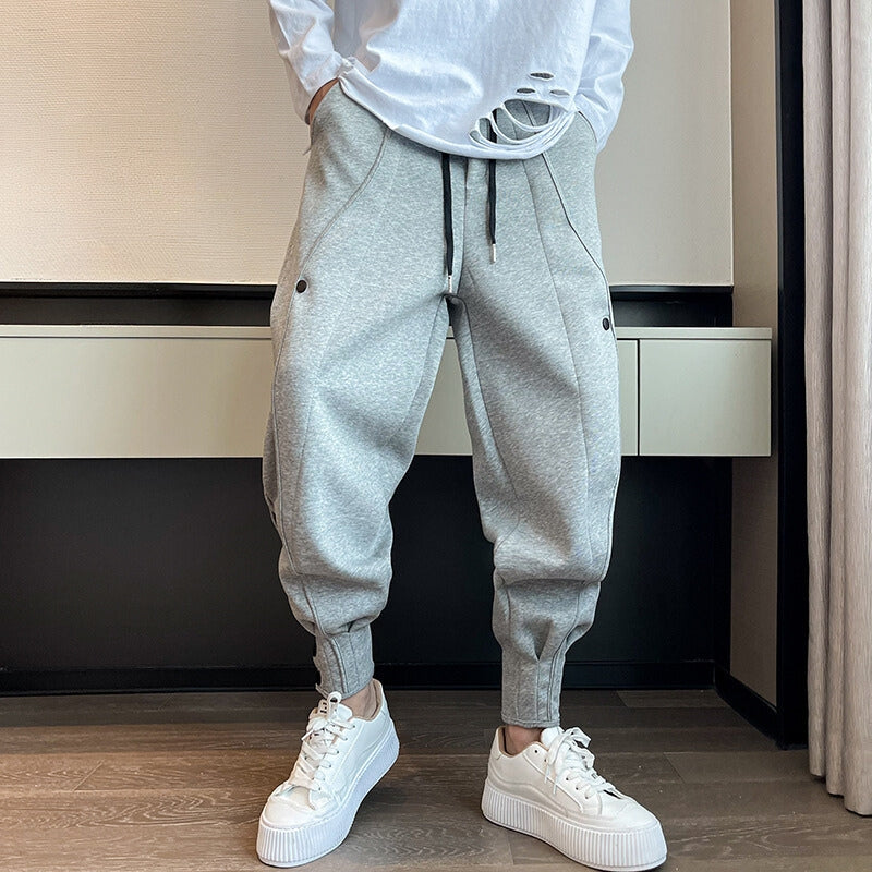 Graue Jogginghose Herren, lässig geschnitten, mit Kordelzug und Taschen, kombiniert mit weißen Sneakers. Moderne Freizeitmode für Männer.