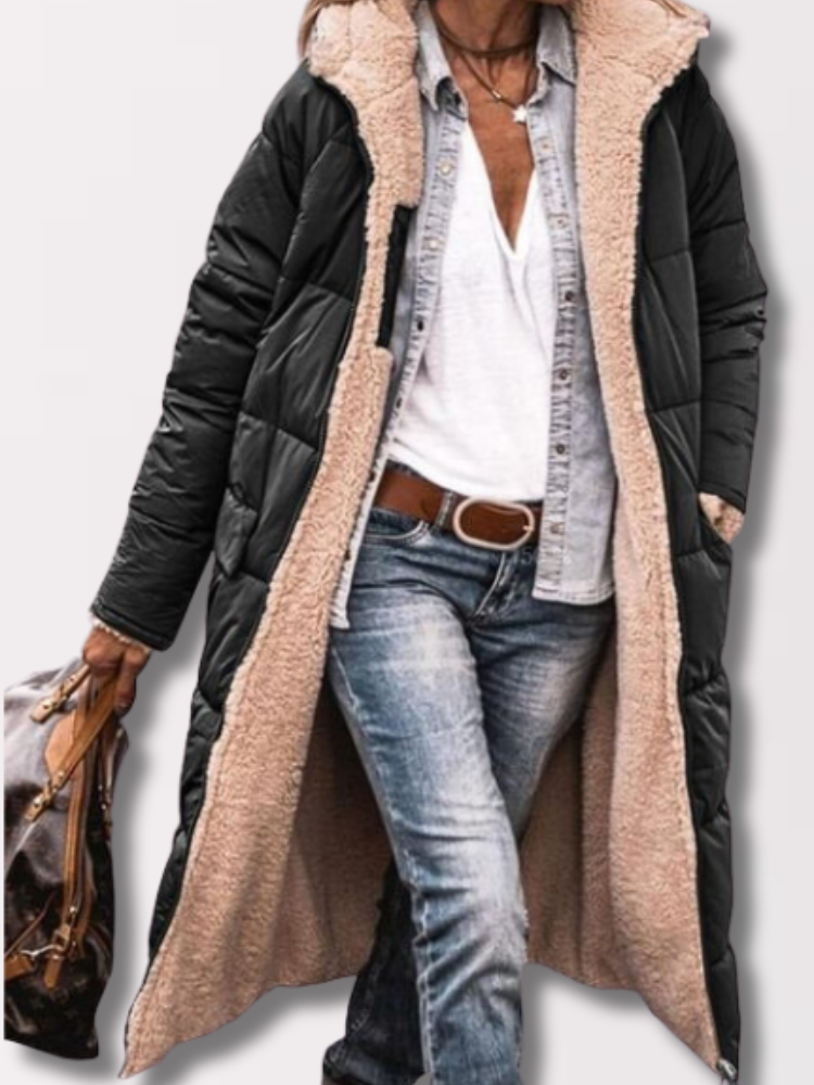 Dame in schwarzem, langem Wintermantel mit beigem Futter, trägt Jeans und weiße Bluse, hält braune Tasche. Modischer Winterlook für Frauen.