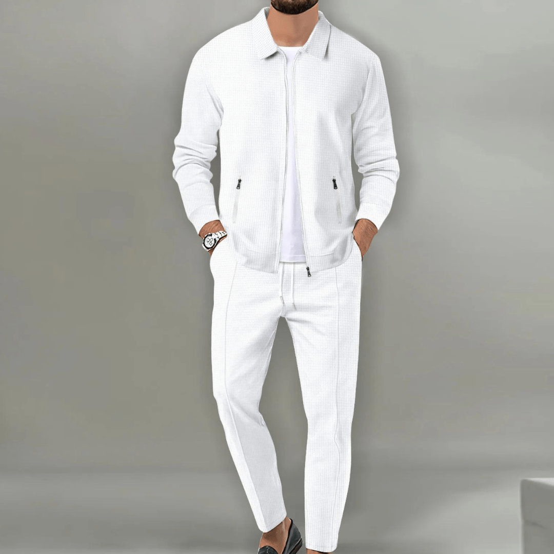 Mann in weißem Anzug mit Reißverschlussjacke und Uhr, modisch elegant, vor grauem Hintergrund. Herrenmode, stilvoll, modern.