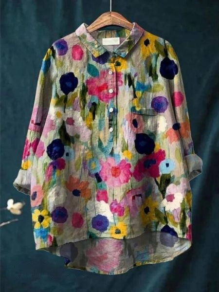 Bunte Damenbluse mit floralem Muster, langen Ärmeln und Knopfleiste, hängend auf einem Kleiderbügel vor dunklem Hintergrund.