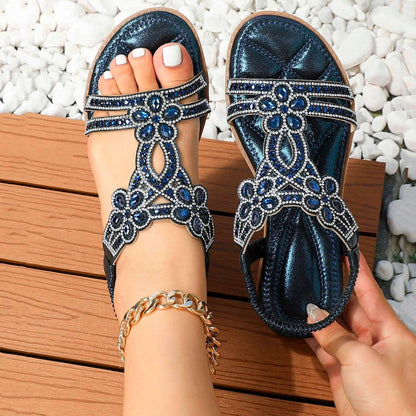 Blaue Sandalen mit Strasssteinen auf Holzterrasse, weiße Pediküre, goldene Fußkette, modische Sommerschuhe, elegantes Design.
