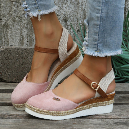 Damen-Sandalen mit Keilabsatz, rosa Wildleder, braune Riemen, weiße Sohle, lässiger Sommerstil, getragen mit zerrissenen Jeans, Outdoor-Hintergrund.