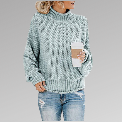 Frau in hellblauem Strickpullover hält Kaffeebecher, trägt zerrissene Jeans. Modetrend, Herbstmode, lässiger Stil, gemütlicher Look.