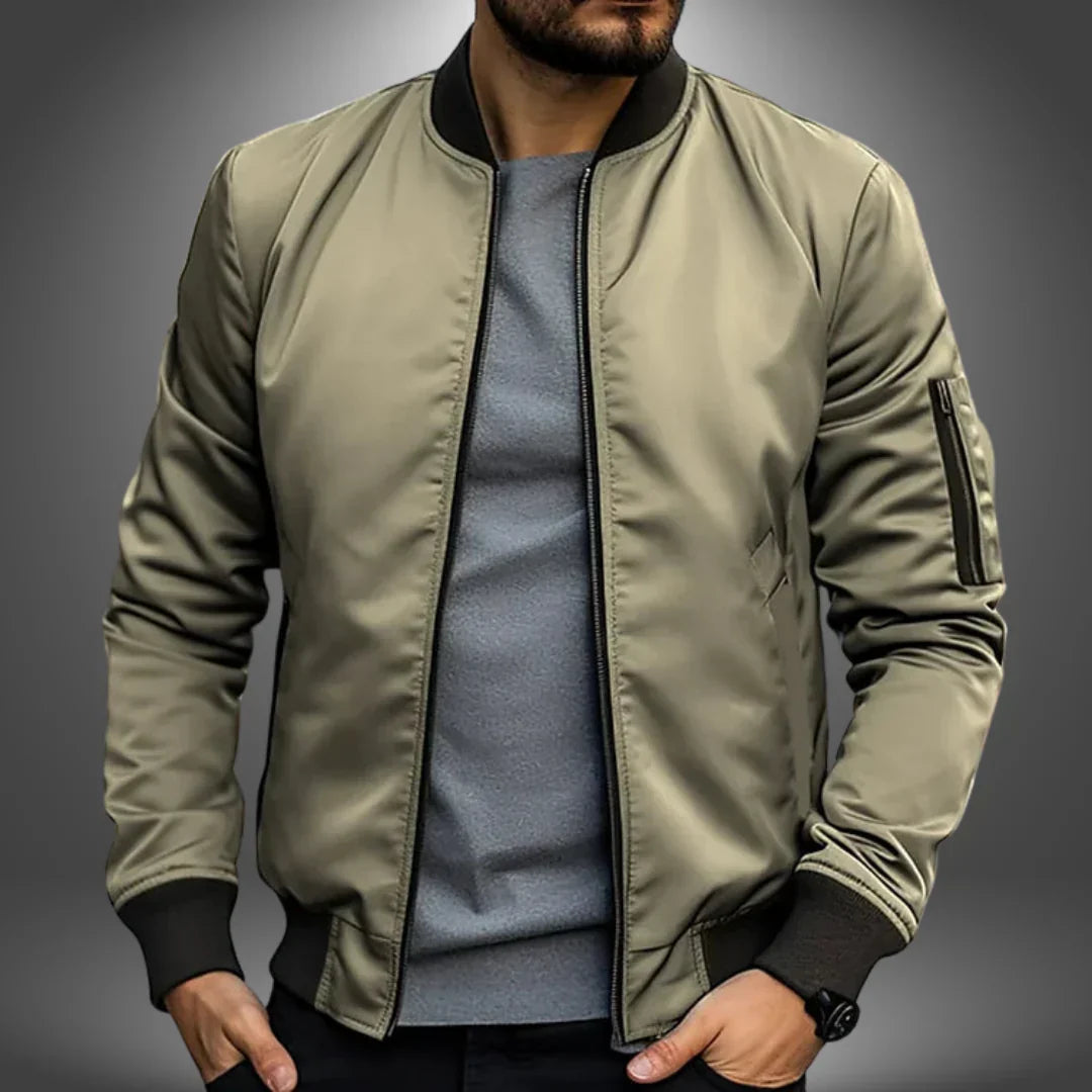 Mann in olivgrüner Bomberjacke, grauem T-Shirt, schwarzer Hose. Modische Herrenbekleidung, lässiger Stil, trendige Jacke, urbaner Look.