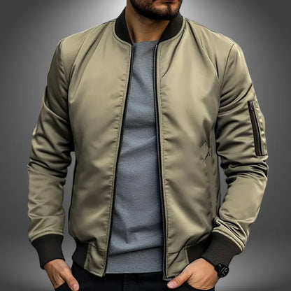 Mann in olivgrüner Bomberjacke, grauem T-Shirt, schwarzer Hose. Modische Herrenbekleidung, lässiger Stil, trendige Jacke, urbaner Look.