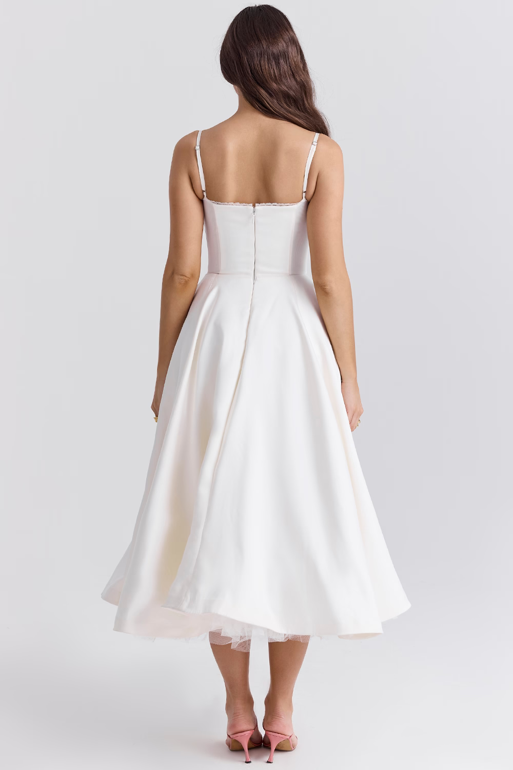 Frau in weißem, ärmellosem A-Linien-Kleid mit Rückenausschnitt, knielang, rosa High Heels, elegantes Abendmode, Hochzeitskleid, Modefotografie.