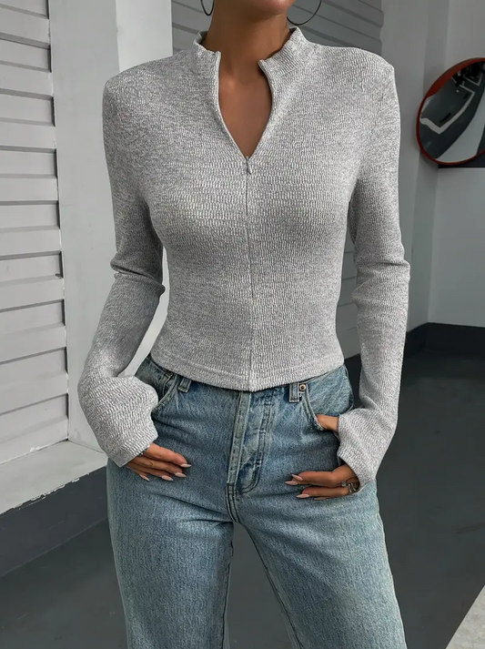 Frau in grauem, langärmligem Oberteil und blauer Jeans, moderne Mode, urbaner Stil, lässiges Outfit, trendige Damenbekleidung.