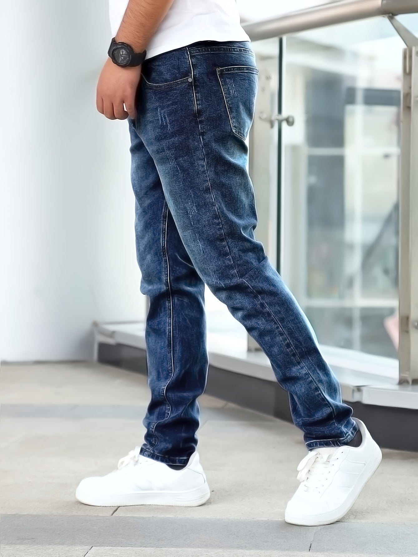 Mann in blauer Jeans und weißen Sneakern steht auf modernem Boden. Lässige Mode, Herrenbekleidung, urbaner Stil, seitliche Ansicht.