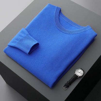 Blauer Pullover aus Kaschmir, gefaltet auf grauem Tisch, neben einer eleganten Armbanduhr mit schwarzem Lederarmband und silbernem Zifferblatt.