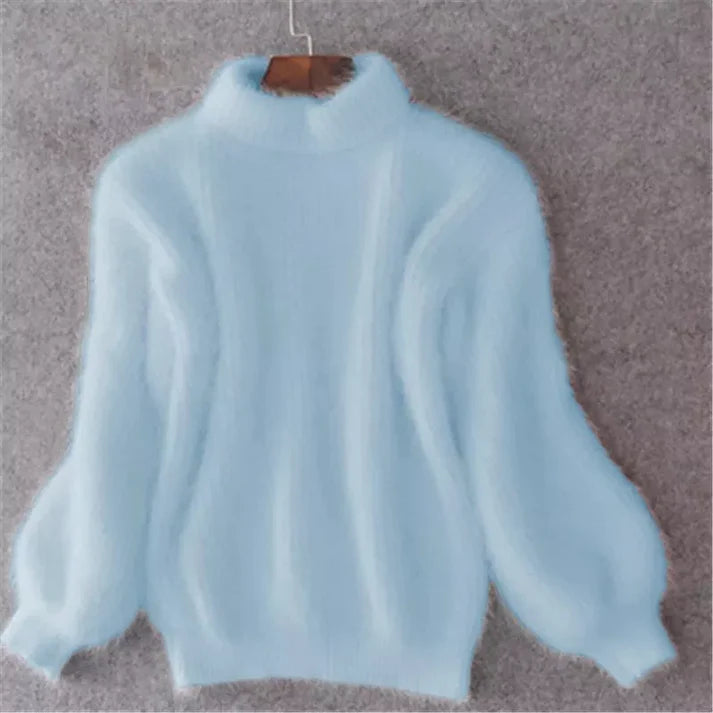 Hellblauer Pullover aus weichem Strick mit Ballonärmeln, hängend an einem Holzbügel vor grauem Hintergrund. Modetrend, Damenbekleidung, Wintermode.
