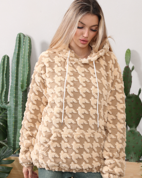 Frau in beigem, flauschigem Hoodie mit Hahnentrittmuster vor Kaktus. Modetrend, gemütlicher Pullover, Herbstmode, Damenbekleidung.