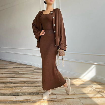 Frau in braunem Strickkleid und Cardigan, hält kleine gesteppte Handtasche, steht auf Holzfußboden. Elegante Herbstmode, stilvoll und modern.