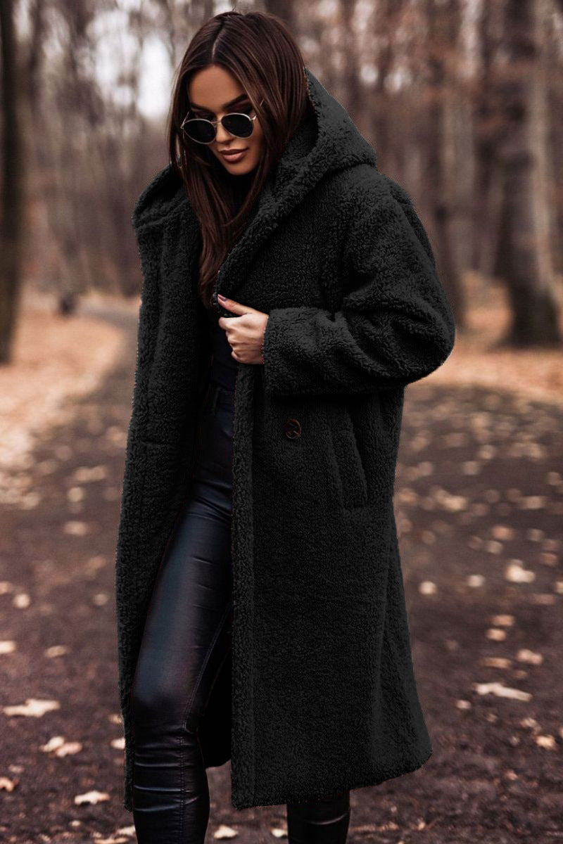 Frau im schwarzen Teddy-Mantel und Sonnenbrille im herbstlichen Wald. Modetrend, Herbstmode, stilvoller Look, Outdoor-Fashion.