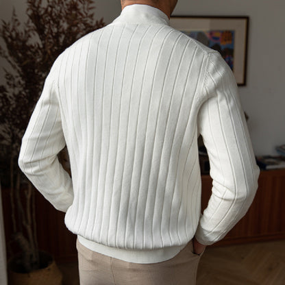 Rückansicht eines Mannes in weißem, geripptem Strickpullover, stehend in modernem Wohnzimmer. Elegante Herrenmode, stilvoller Winterlook.