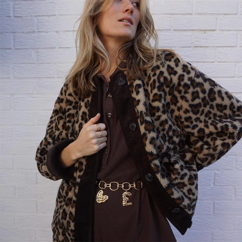 Frau in Leopardenmuster-Jacke vor weißer Ziegelwand, trägt braunes Kleid und goldene Gürtelkette. Modetrend, Herbstmode, Streetstyle.