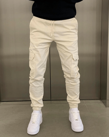 Beige Cargo-Hose mit Taschen, getragen von einer Person, kombiniert mit weißen Sneakers. Modetrend, lässiger Stil, Herrenbekleidung.