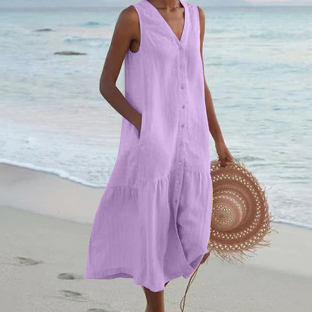 Frau am Strand in lila Sommerkleid, hält Strohhut. Strandmode, Sommeroutfit, Freizeitkleidung. Ideal für Urlaub am Meer.