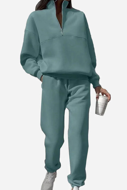Frau in mintgrünem Jogginganzug mit Reißverschluss, hält Kaffeebecher. Bequeme Freizeitmode, sportlicher Look, trendige Damenbekleidung.