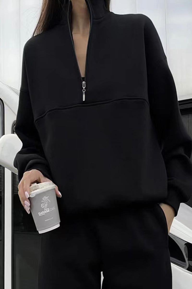 Frau in schwarzem Pullover mit Reißverschluss hält einen Kaffeebecher. Moderne Freizeitmode, urbaner Stil, lässiges Outfit.