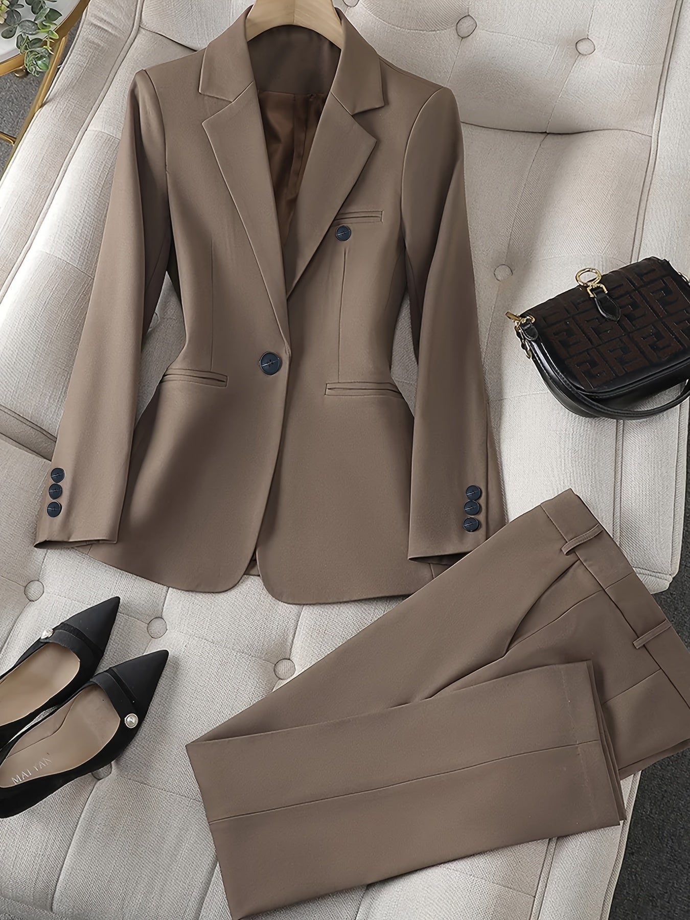 Damenanzug in Beige auf Sofa, bestehend aus Blazer und Hose, mit schwarzen Pumps und Designerhandtasche. Elegante Businessmode für Frauen.