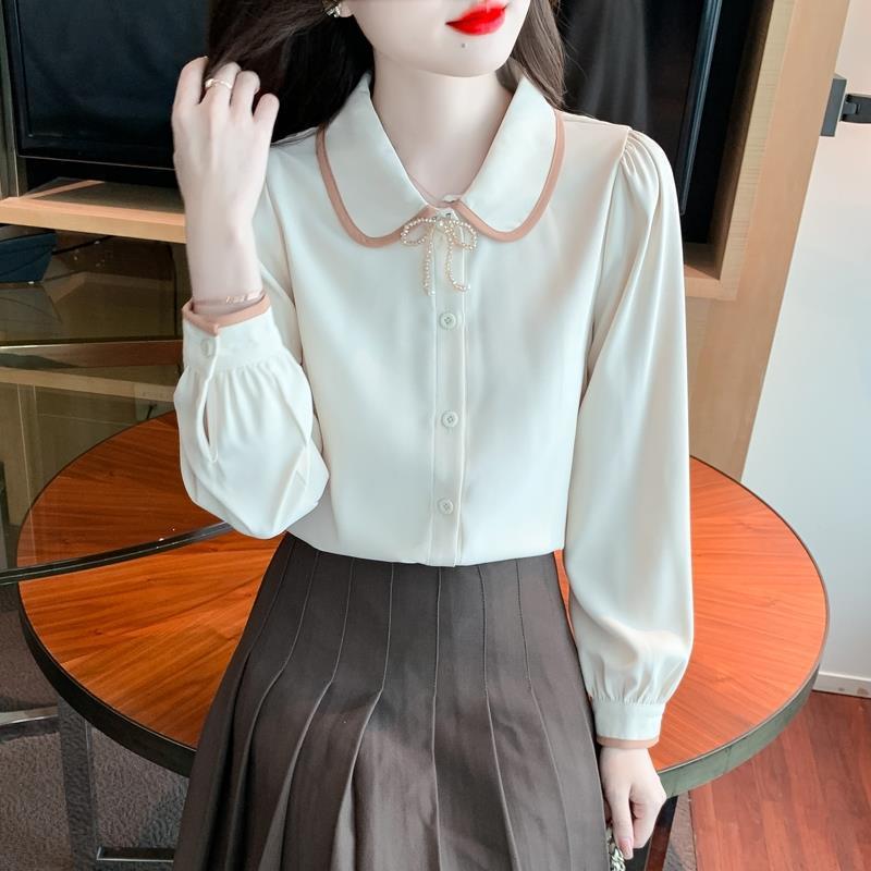 Frau in eleganter Bluse mit Schleifenkragen und braunem Faltenrock sitzt an Holztisch. Modetrend, Damenmode, stilvolle Kleidung.