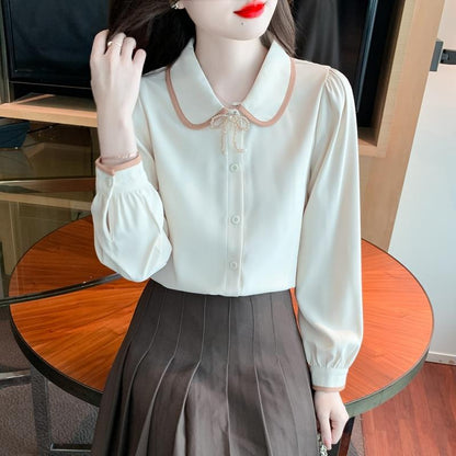 Frau in eleganter Bluse mit Schleifenkragen und braunem Faltenrock sitzt an Holztisch. Modetrend, Damenmode, stilvolle Kleidung.